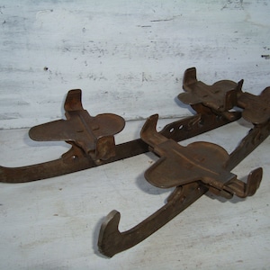 May include: A pair of vintage rusty metal ice skates with a clamp-on design. The skates have a metal blade and a metal foot strap.