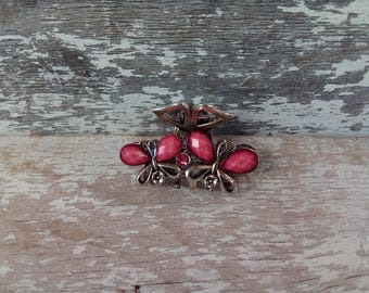 May include: A silver-coloured hair clip with a butterfly design and pink gemstone accents. The clip has a decorative top and two butterfly-shaped elements with pink, oval-shaped stones.