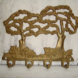 May include: Brass key holder shaped like two stylized trees with five hooks. The trees are intricately detailed with leaves and branches.