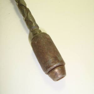 May include: A close-up of a metal drill bit with a twisted shaft and a metal chuck. The drill bit is rusty and has a worn finish.
