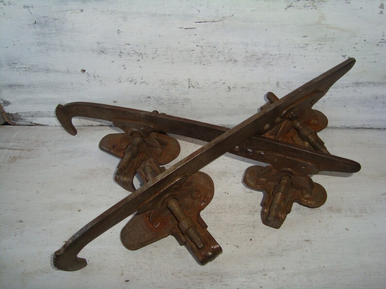 May include: A pair of vintage rusty metal ice skate blades with a hook on each end. The blades are attached to a metal base with screws.