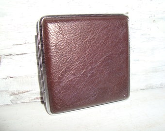 May include: A brown leather cigarette case with a silver metal frame.