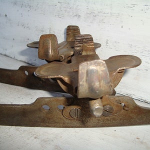 May include: A pair of vintage rusty metal ice skate blades with a metal toe stop. The blades are attached to a metal frame with a screw.