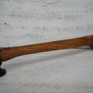 May include: A vintage hammer with a wooden handle and a black metal head. The hammer has a rounded head and a slightly curved handle.