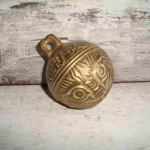 May include: A small, round, brass bell with an intricate design. The bell has a loop at the top for hanging.