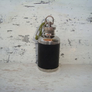 Op de afbeelding: Een zilveren en zwarte metalen fles met een groene karabijnhaak. De fles heeft een getextureerde zwarte afwerking en een zilveren dop.