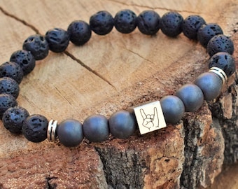 May include: Black lava rock and dark grey hematite bead bracelet with a silver charm featuring a rock and roll hand gesture.