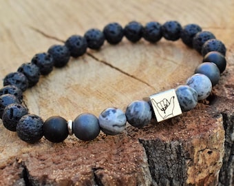 May include: Black lava rock and grey agate beaded bracelet with a silver charm featuring a hand gesture.