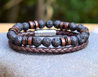 Op de afbeelding: Een bruin leren armband met een zwarte lava- en houten kralen armband eroverheen gelegd. De armband heeft een magneetsluiting.