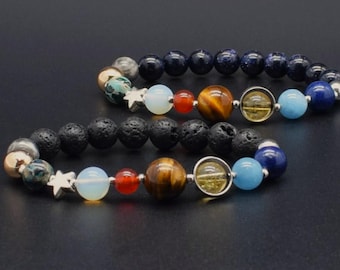 May include: Two beaded bracelets featuring a solar system design. One bracelet uses dark blue glitter beads, while the other uses black porous lava beads. Both include a variety of colored gemstone beads representing planets, a silver star charm, and a ringed bead.