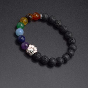 May include: A beaded bracelet featuring black porous lava stone beads and a series of smooth, multi-colored gemstone beads. A silver-toned metal charm shaped like a paw print with the letter D engraved in the center is integrated into the design.