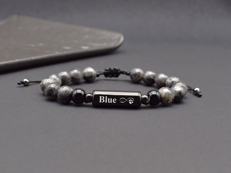 May include: Black beaded bracelet with a black metal charm engraved with the word "Blue" and an infinity symbol with a paw print.