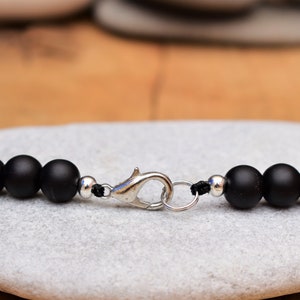 May include: A black beaded bracelet with a silver clasp. The bracelet is made of matte black beads and has a simple design.