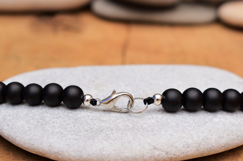 May include: A black beaded bracelet with a silver clasp. The bracelet is made of matte black beads and has a simple design.