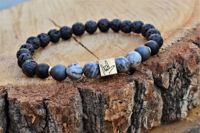 May include: Black lava rock and grey agate beaded bracelet with a silver charm featuring the American Sign Language symbol for "I love you".