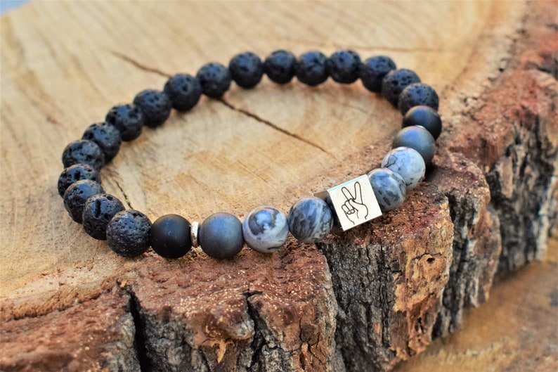 May include: Black lava rock and grey stone beaded bracelet with a silver charm featuring a peace sign.