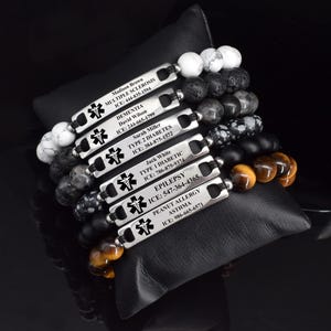 May include: A collection of six medical alert bracelets featuring silver-toned rectangular metal plates engraved with a medical caduceus symbol, names, conditions, and ICE contact numbers, strung with various natural stone beads in white, black, and brown.
