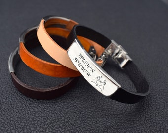 May include: Three leather bracelets with a silver clasp and a silver plate engraved with the coordinates "78°53'31"N 55°11'61"W" and a heart symbol.