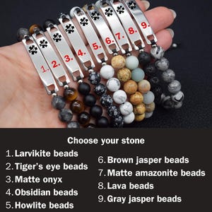 May include: Nine medical alert bracelets featuring silver-tone metal plates with a black Star of Life symbol. Each bracelet has a unique stone bead strand: larvikite, tiger's eye, matte onyx, obsidian, howlite, brown jasper, amazonite, lava, and gray jasper.