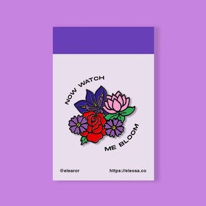Könnte beinhalten: Eine farbige Emaille-Anstecknadel mit einem Blumenstrauß und dem Text "NOW WATCH ME BLOOM".