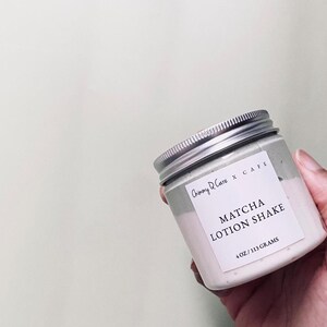 May include: A white jar with a silver lid containing a green and white lotion. The jar has a label that reads "Chimmy D'Care x CAFE MATCHA LOTION SHAKE 4 OZ / 113 GRAMS".