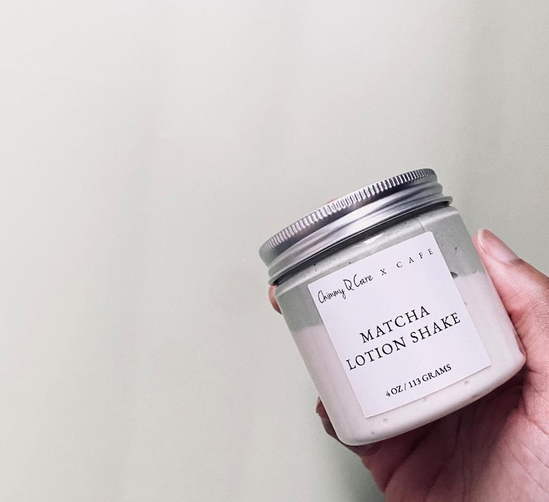 May include: A white jar with a silver lid containing a green and white lotion. The jar has a label that reads "Chimmy D'Care x CAFE MATCHA LOTION SHAKE 4 OZ / 113 GRAMS".
