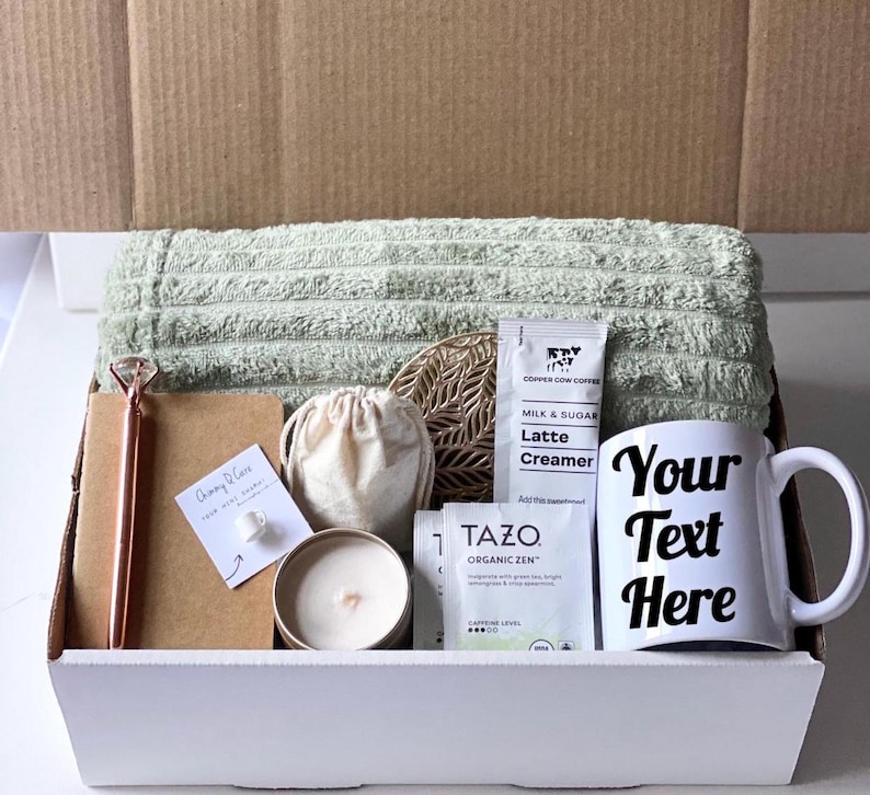 May include: A white gift box filled with a green towel, a candle, a small bag, a notebook with a pen, a coaster, a coffee creamer packet, a tea bag, and a white mug with the text "Your Text Here".