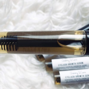 May include: A clear plastic tube with a black applicator brush filled with a light brown liquid. The tube is labeled "Eyelash Growth Serum".