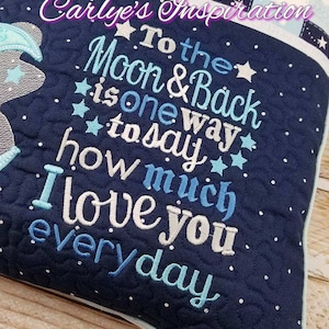 May include: A blue and white quilted cushion with the text "To the Moon & Back is one way to say how much I love you everyday" embroidered on it.