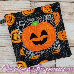 Puede incluir: Manopla de cocina negra y naranja con temática de Halloween con una gran cara de calabaza bordada y un patrón de telaraña.