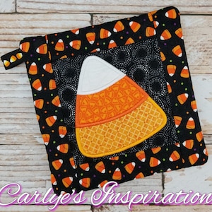 Könnte beinhalten: Ein schwarzer und orangefarbener Topflappen im Halloween-Design mit einem Mais-Motiv. Der Topflappen hat eine Aufhängeschlaufe und ist mit einem schwarzen Hintergrund und orange-weißen Mais verziert.