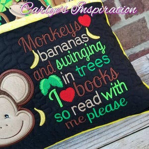 May include: A black and yellow pillow with embroidered monkeys, bananas, and the text "Monkeys bananas and swinging in trees I love books so read with me please".