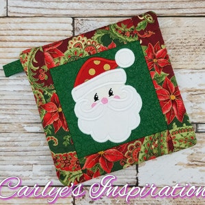 May include: A square Christmas potholder with a Santa Claus applique on a green centre. The Santa has a white beard and a red hat with gold spots. The border features red poinsettias and green paisley patterns. The text "Carlye's Inspiration" is at the bottom.
