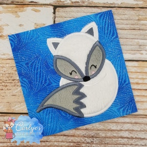 May include: A white and gray embroidered arctic fox with a blue sparkly background. The fox is curled up with its tail covering its face.