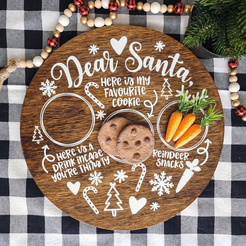 May include: A wooden round serving tray with a white painted design for Santa. The tray has a place for a cookie, a drink, and reindeer snacks. The text on the tray reads "Dear Santa, Here is my favourite cookie. Here is a drink incase you're thirsty. Reindeer Snacks."