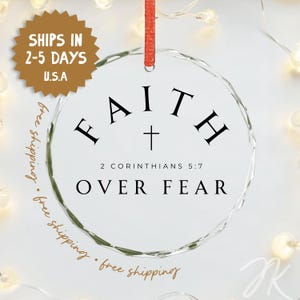 Könnte beinhalten: Ein kreisförmiges Ornament aus klarem Glas mit facettierten Kanten und einem roten Band zum Aufhängen. Der Text FAITH ist in Schwarz über einem kleinen Kreuz gedruckt, gefolgt von 2 CORINTHIANS 5:7 und dem Text OVER FEAR in schwarzen Großbuchstaben.