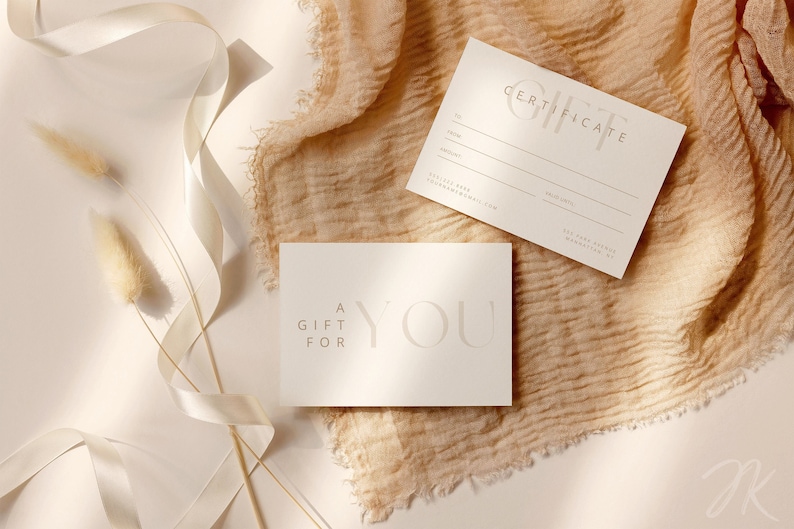 May include: Two off-white gift cards with elegant, minimalist design. One card reads "A Gift For You" and the other is a gift certificate. The cards are on a beige fabric with decorative elements.