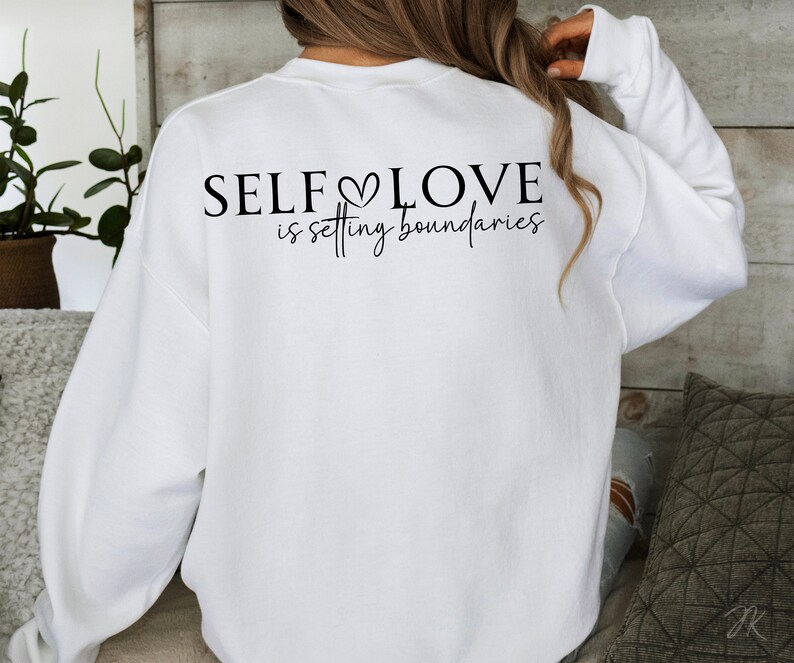 Puede incluir: Sudadera blanca con el texto "SELF LOVE is setting boundaries" impreso en la espalda.