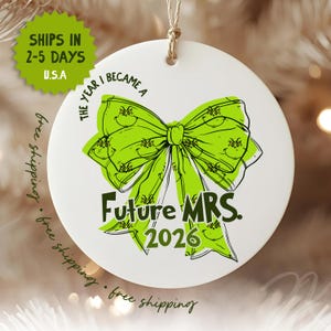May include: A round white ceramic ornament featuring a bright lime green bow graphic with a repeating character face pattern. The text reads THE YEAR I BECAME A Future MRS. 2026 in black lettering. The ornament hangs from a thin tan twine loop.
