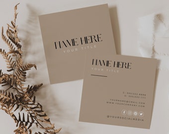 May include: Two square business cards with a taupe background. The top card reads "NAME HERE" and "YOUR TITLE" in black font. The bottom card includes contact information, social media icons, and the same text. A dried fern and white fabric are in the background.
