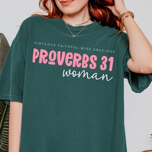 K&ouml;nnte beinhalten: Ein tealgr&uuml;nes T-Shirt mit dem Text "PROVERBS 31 woman" in rosa Schrift. Der Text "VIRTUOUS. FAITHFUL. WISE. GRACIOUS" ist in wei&szlig; &uuml;ber dem Haupttext gedruckt.