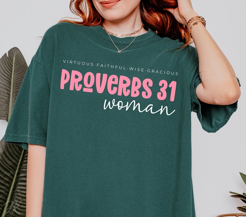 K&ouml;nnte beinhalten: Ein tealgr&uuml;nes T-Shirt mit dem Text "PROVERBS 31 woman" in rosa Schrift. Der Text "VIRTUOUS. FAITHFUL. WISE. GRACIOUS" ist in wei&szlig; &uuml;ber dem Haupttext gedruckt.