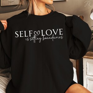 Puede incluir: Sudadera negra con texto blanco que dice "SELF LOVE is setting boundaries".