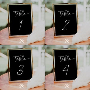 May include: Four gold-framed black table number signs with white calligraphy. The signs read "table 1", "table 2", "table 3", and "table 4".