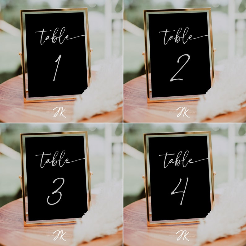 May include: Four gold-framed black table number signs with white calligraphy. The signs read "table 1", "table 2", "table 3", and "table 4".