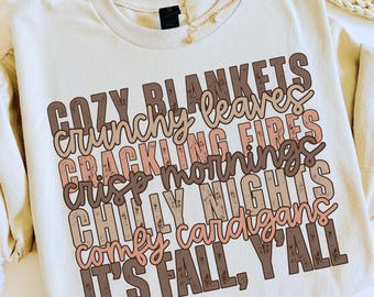 May include: Cream-colored sweatshirt with the text "COZY BLANKETS, CRUNCHY LEAVES, CRACKLING FIRES, CRISP MORNINGS, CHILLY NIGHTS, COMFY CARDIGANS, IT'S FALL, Y'ALL" in brown and pink lettering. A gold necklace is visible.