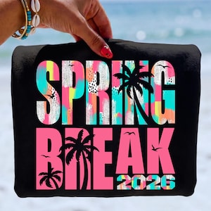 May include: Black beach towel with the words "SPRING BREAK 2026" in large, colorful letters. The word "SPRING" is in white with a colorful background, and "BREAK" is in pink. Palm tree silhouettes and birds are also featured.