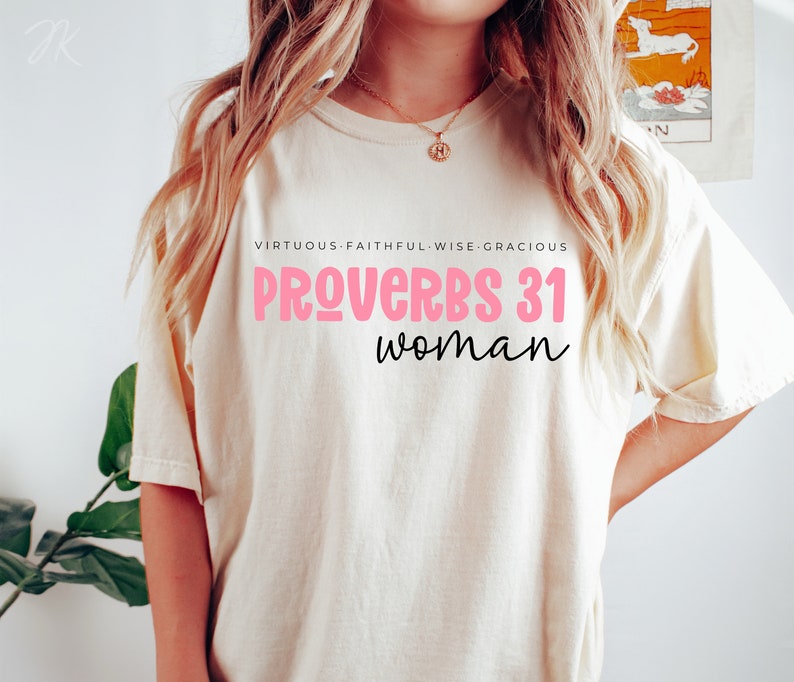 K&ouml;nnte beinhalten: Ein wei&szlig;es T-Shirt mit dem Text "SPR&Uuml;CHE 31 Frau" in rosa und schwarzer Schrift. Der Text "TUGENDHAFT - TREU - WEISE - GN&Auml;DIG" steht in Schwarz &uuml;ber dem Haupttext.