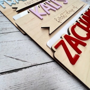 May include: Three wooden signs with the names Frankie, Kail, and Zachariah, each with the text "first day of" in cursive. The signs are stacked on top of each other, with Frankie's sign on top and Zachariah's sign on the bottom. The names are in different colors: Frankie's name is light blue, Kail's name is pink, and Zachariah's name is red.
