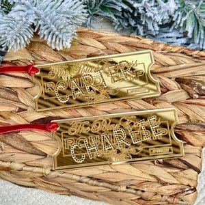 May include: Two gold-coloured ticket ornaments with red ribbon ties. The tickets read "The Polar Express Round Trip" and have ticket numbers.